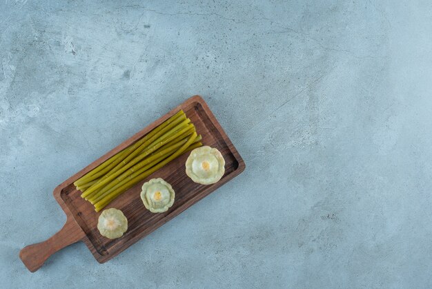 Delicious pickled mini squash and sticks on a board, on the marble table. 