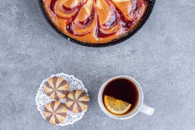 Delicious pie with berry, biscuits and cup of tea on marble surface