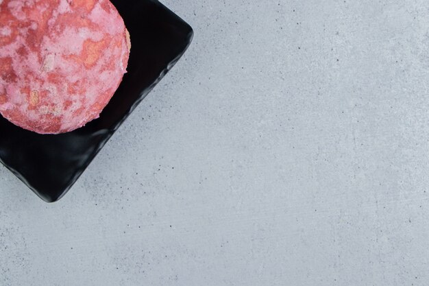 A delicious pink cookie on a black platter on marble background.