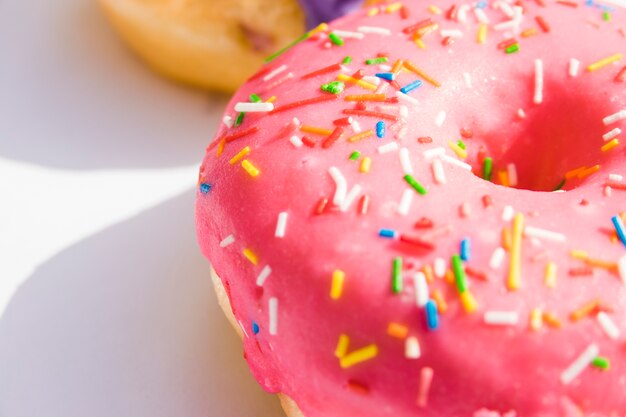 Delicious pink donuts with sprinkles on white desk