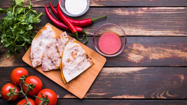 Delicious pita on chopping board near sauces among vegetables and herbs