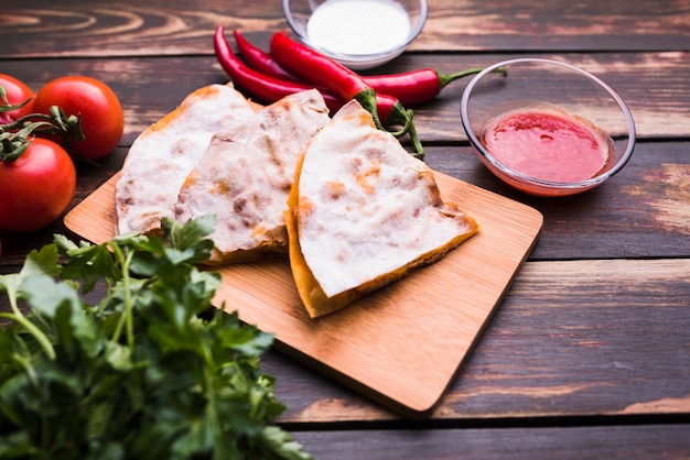 Delicious pita on cutting board near sauces among vegetables