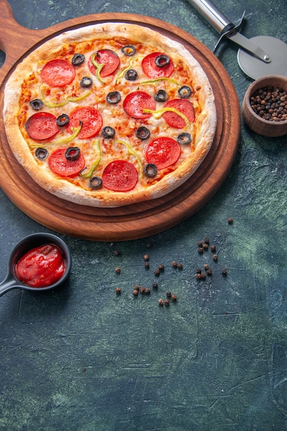 Delicious pizza on wooden cutting board and pepper ketchup on isolated dark surface in vertical view