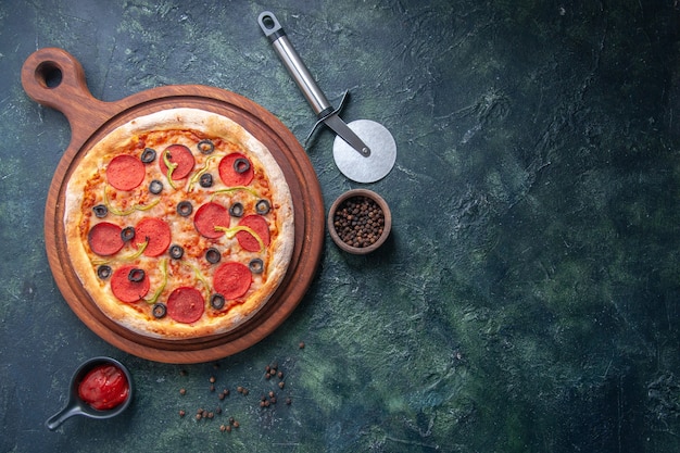 Вкусная пицца на деревянной разделочной доске и перцовый кетчуп с правой стороны на изолированной темной поверхности