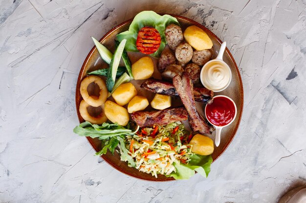 Delicious restaurant appetizers set for beer vegetable salad boiled potatoes grilled chicken legs roasted onion sausages cucmbers tomatoes and sauces ketchup and mayo laying on clay plate