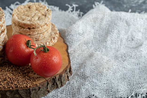 Delicious rice cakes, tomatoes and raw buckwheat on wooden piece