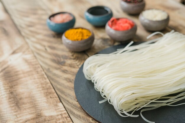 Delicious rice noodles and ingredients in bowl on old wooden texture plank