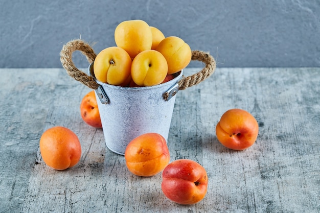 Delicious ripe apricots in iron bucket with nectarines on marble surface