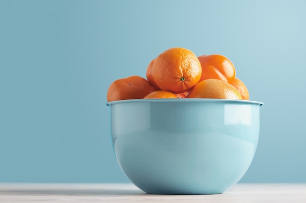 Delicious ripe fresh fruits and citruses in blue metallic bowl isolated on white tooden table on pastel blue background: persimmon, date plum, mandarine, orange, grapefruit, pomelo