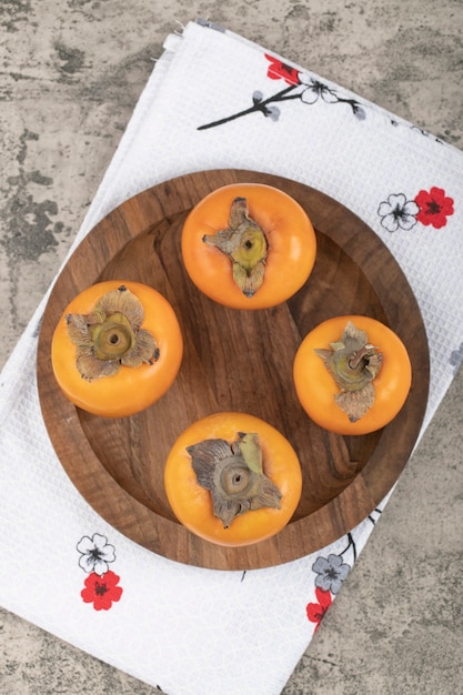 Foto gratuita deliziosi frutti di cachi maturi posti su un piatto di legno
