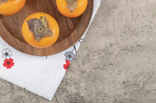 Delicious ripe persimmon fruits placed on wooden plate