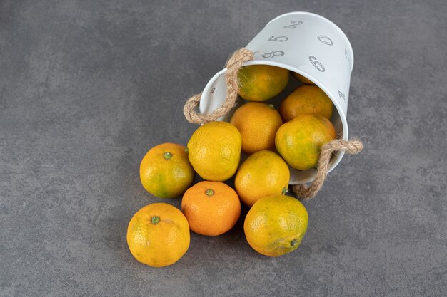 Delicious ripe tangerines out of bucket on marble background. High quality photo
