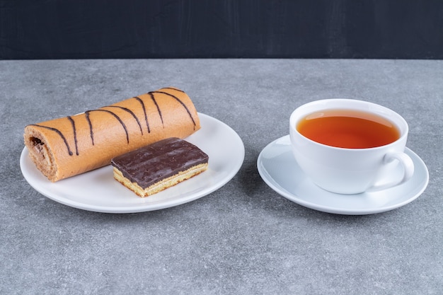 Delicious roll cake with chocolate cake on white plate and cup of tea