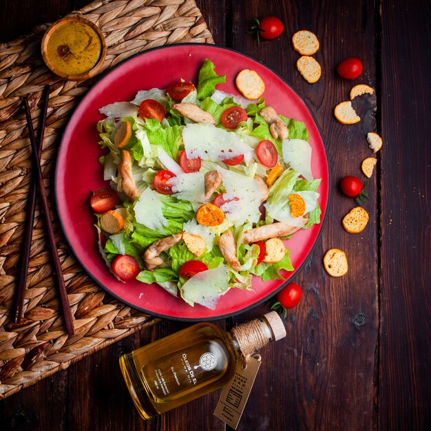 Delicious salad in a red plate with oil on wooden background, flat lay.
