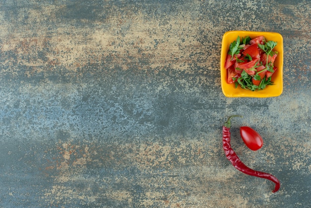 Free photo delicious salad in yellow plate with pepper and tomato on marble background