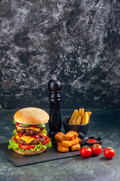 Вкусный сэндвич и куриные наггетсы фри на темном подносе с помидорами на черной поверхности в вертикальном виде
