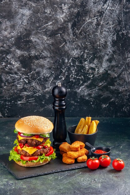 Вкусный сэндвич и куриные наггетсы фри на темном подносе с помидорами на черной поверхности в вертикальном виде