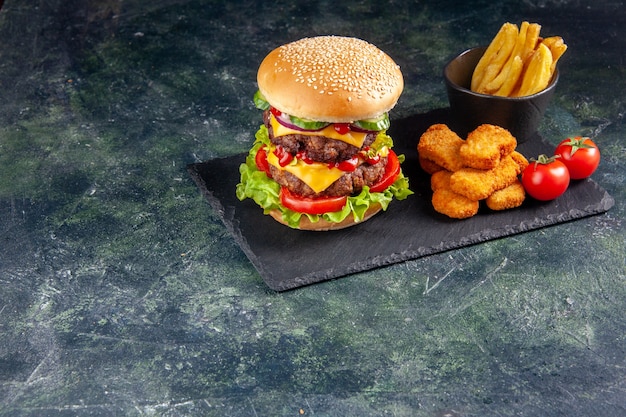 Delicious sandwich on dark color tray and chicken nuggets tomatoes fries on the left side on black surface