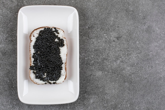 Free photo delicious sandwich with black caviar on white plate over grey surface