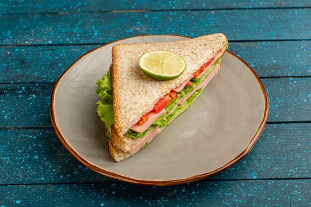delicious sandwich with green salad tomatoes and ham inside plate on blue