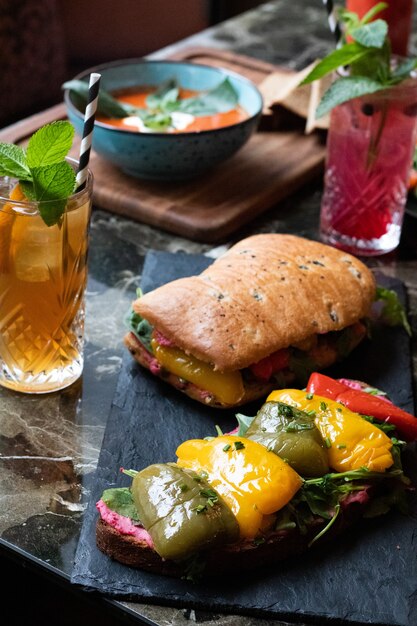 Delicious sandwich with sauce, greens, roasted bell peppers and glasses of fresh juice with straws