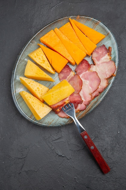 Foto gratuita deliziosa fetta di salsiccia e formaggio su un piatto blu su sfondo scuro