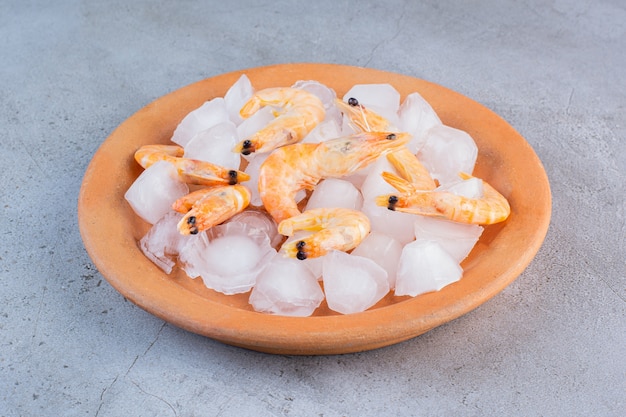 Бесплатное фото Вкусные креветки в кубиках льда в оранжевой тарелке на каменной поверхности