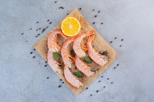 Delicious shrimps with sliced lemon and peppercorns on greaseproof paper .