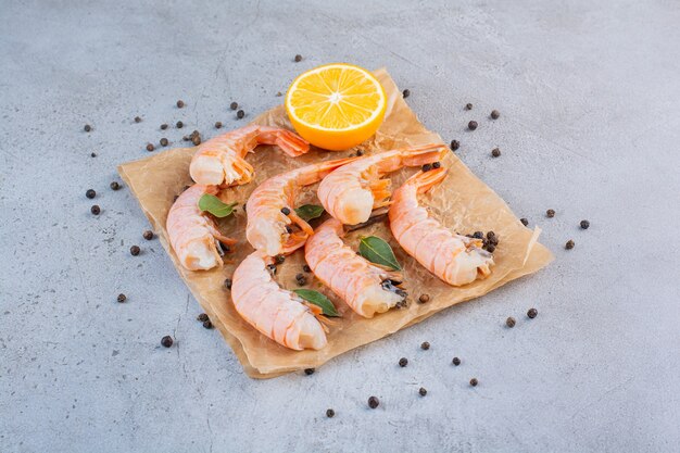 Delicious shrimps with sliced lemon and peppercorns on greaseproof paper .