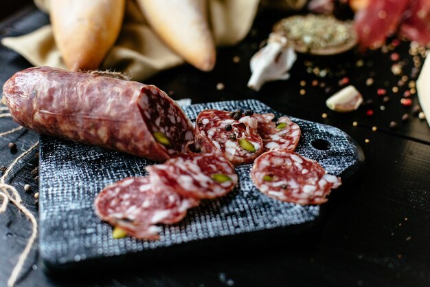 Delicious sliced Italian sausage with pistachios and spice on black cutting board