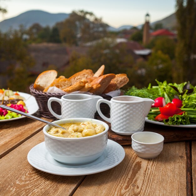 Delicious soup meal with bread, greens, salad in a bowl with village on background, high angle view.