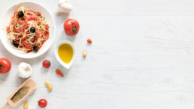 접시에 맛있는 스파게티 파스타; 신선한 토마토; 올리브 오일과 나무 책상에 허브의 그릇