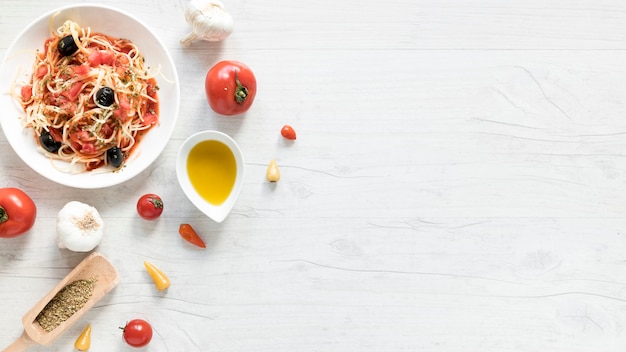 Вкусные макароны спагетти на тарелке; свежий помидор; миска оливкового масла и травы на деревянный стол