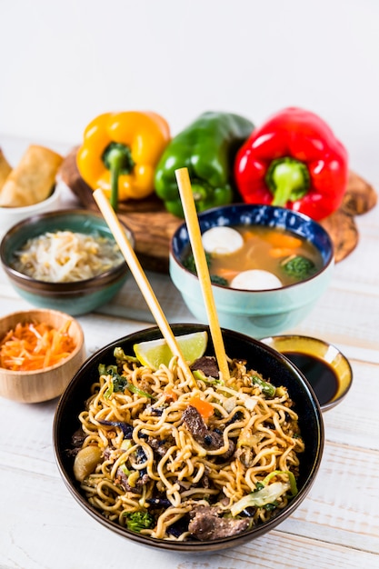 Delicious stir fry noodles with beef on chopsticks with soup bowl over the wooden desk