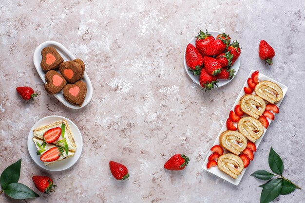 Delicious strawberry cake roll, heart shaped cookies, cake slices with fresh strawberries, top view