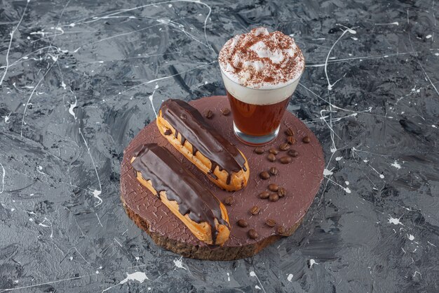 Delicious sweet chocolate eclairs and cup of coffee on wood piece. 