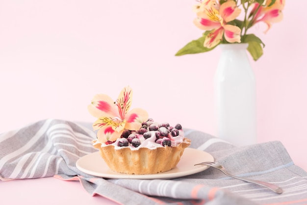 Delicious tart with blueberries and alstroemeria flower on ceramic plate against pink backdrop