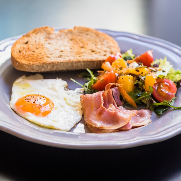 Delicious toast; half fried egg; bacon and salad on gray plate