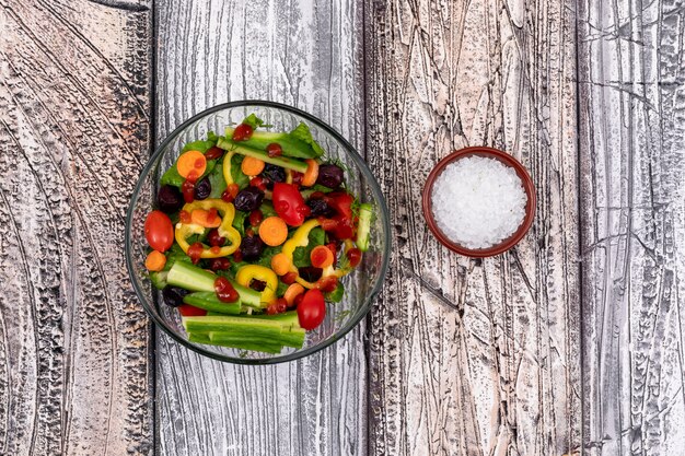 Delicious vegetable salad with cucumber, tomato, pepper and olive, and bowl of salt