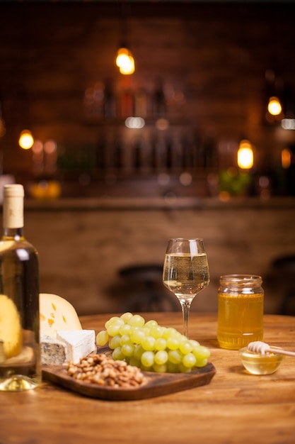 Delicious white grapes on a rustic wooden platter next to tasty walnuts. Wine degustation. Different tasty cheeses.