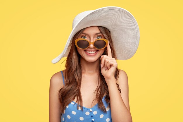 Delighed young woman wearing a hat posing against the yellow wall