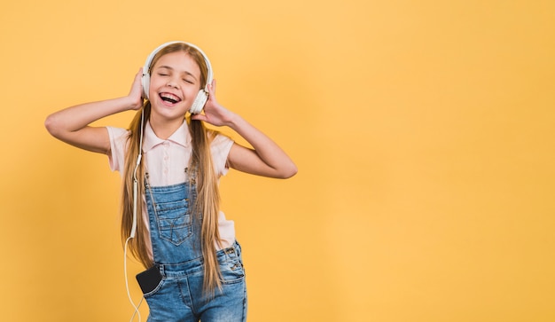 Восхитительная девушка наслаждается прослушиванием музыки на наушниках на желтом фоне