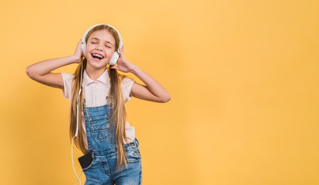 Delight girl enjoying listening the music on headphone against yellow backdrop