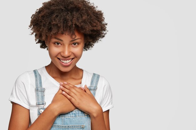 喜んでいる黒人の10代の少女は歯を見せる笑顔を持っており、両手を胸に保ちます