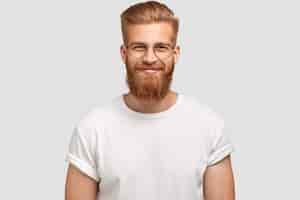 Free photo delighted cheerful fashionable hispster with ginger beard, wears round spectacles and white t shirt