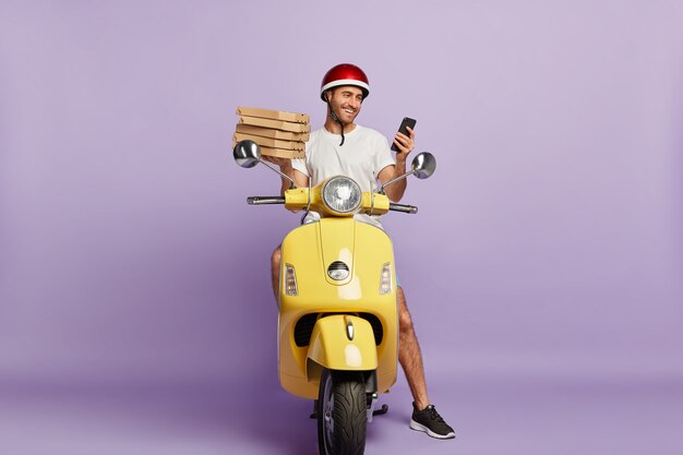 Delighted deliveryman driving scooter while holding pizza boxes