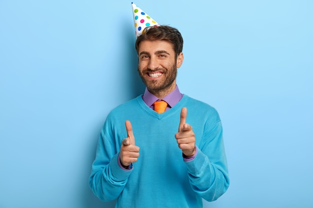 青いセーターでポーズをとって誕生日の帽子をかぶった喜んでいる男