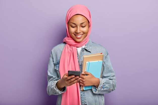 기뻐하는 무슬림 여학생이 소셜 네트워크에서 사진을보고, 최신 셀룰러를 보유하고, 재미있는 비디오 콘텐츠를 시청합니다.