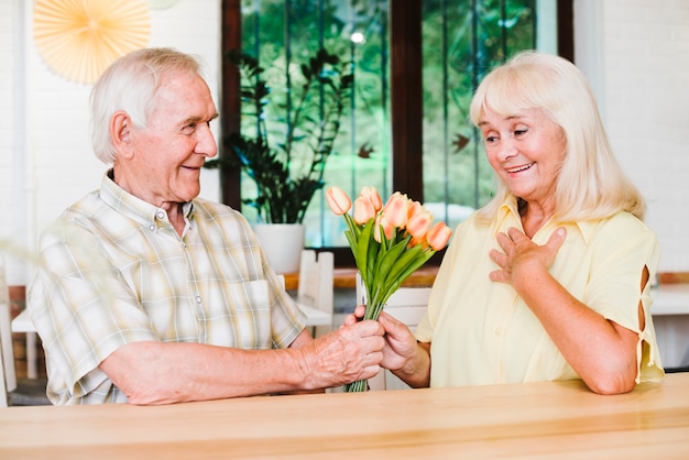 Delighted senior couple sitting in cafe and presenting flowers