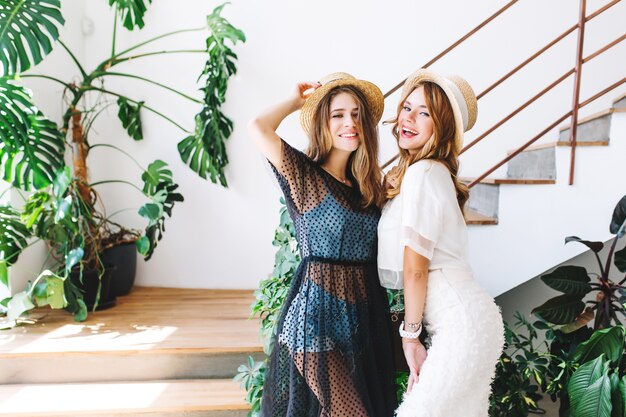 Delighted stylish girls in hats having fun together and dancing beside wooden steps